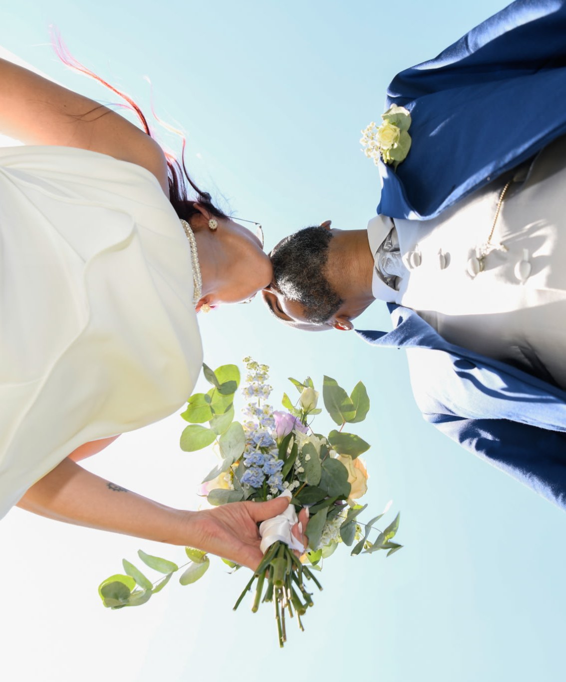 Des mariés et leur bouquet, photographiés en contre-plongée
